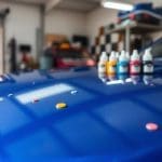 Blue car hood with paint chips and color-matching paint bottles, illustrating collision repair and paint damage assessment.