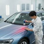 Technician applying paint to a car's surface in an auto body repair shop, illustrating collision repair and repainting services in San Antonio.