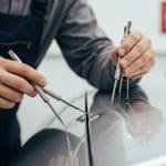 Technician performing paintless dent repair on a car, using specialized tools to maintain the vehicle's original paint finish, emphasizing quick and affordable collision repair services.